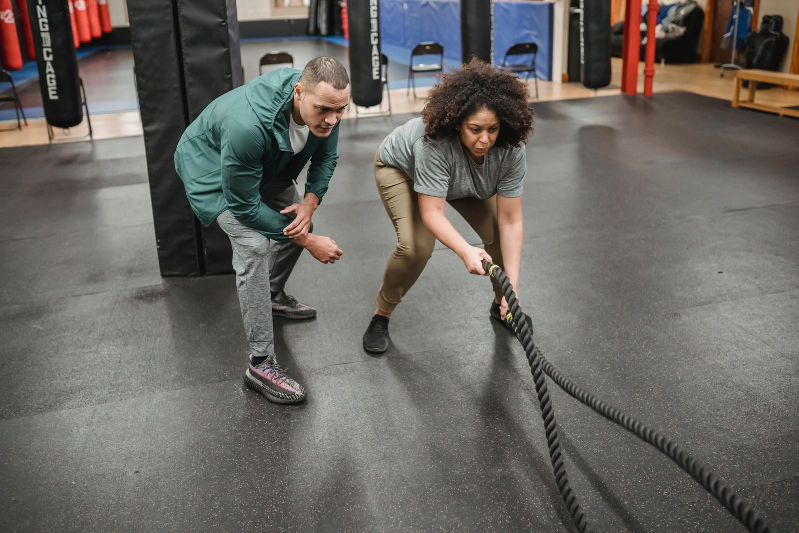 A coach guiding a woman through a workout with battle ropes.